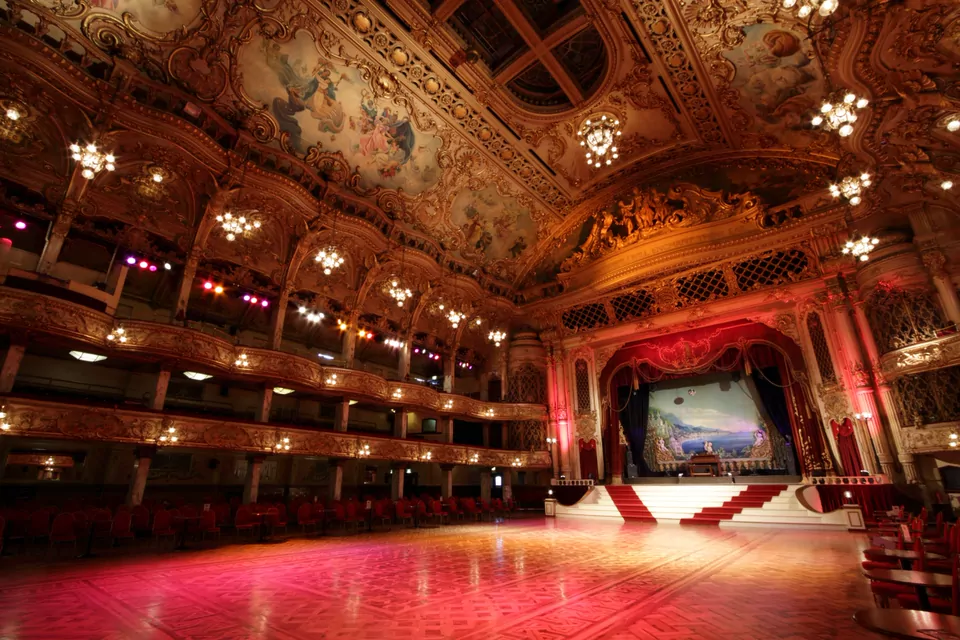 Ornate golden ballroom with a stage, red curtains and warm lights