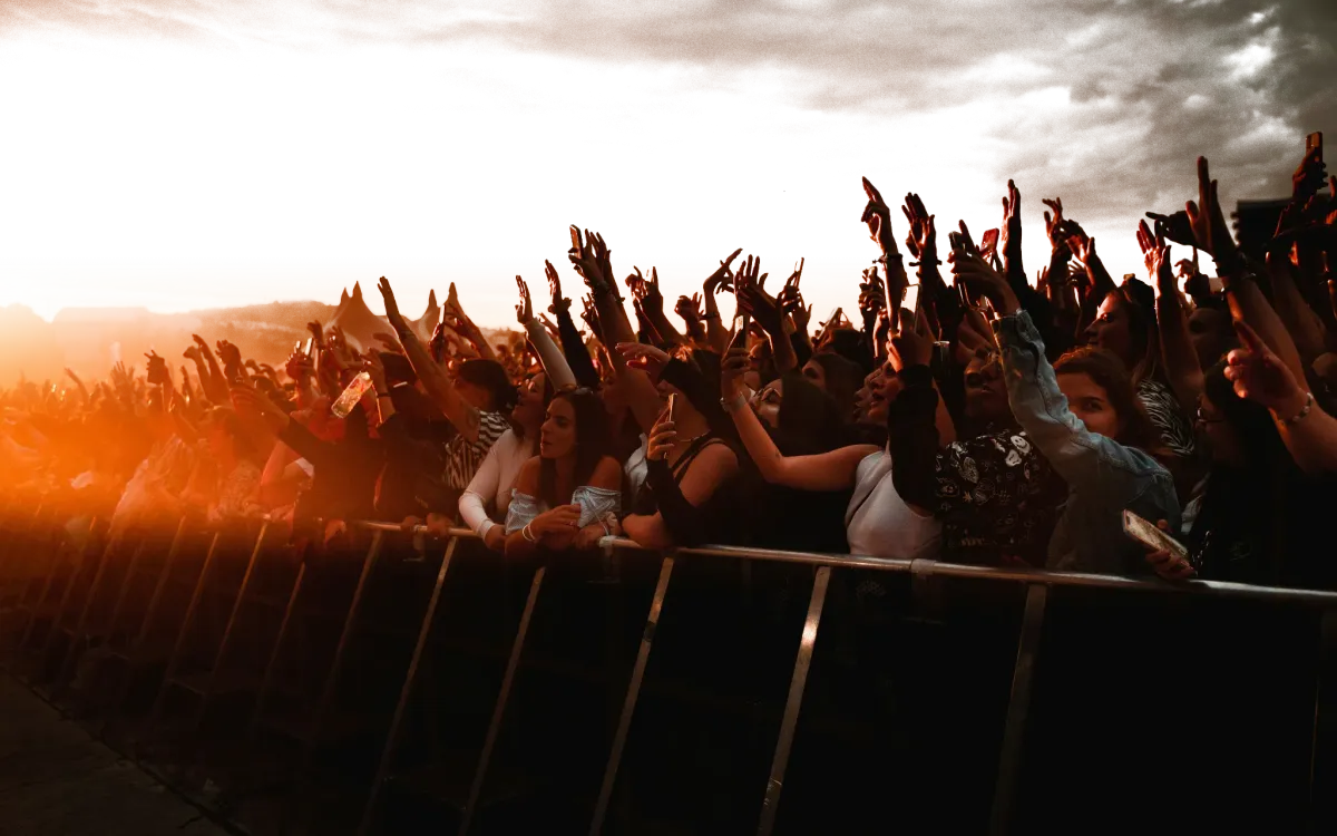 A festival crowd pressed to the barrier at sunset, hands in the air, the light low and warm behind them.