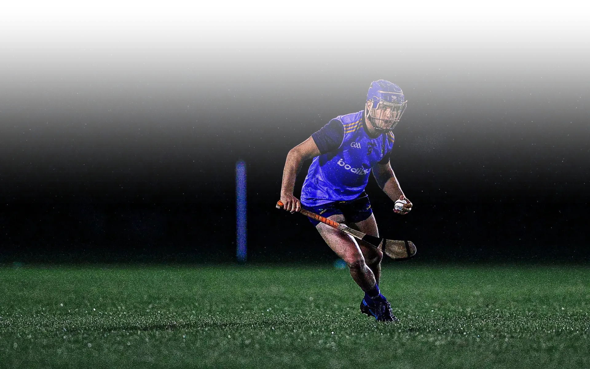 A hurler running with the ball under floodlights, the pitch dark around him and snow in the air.